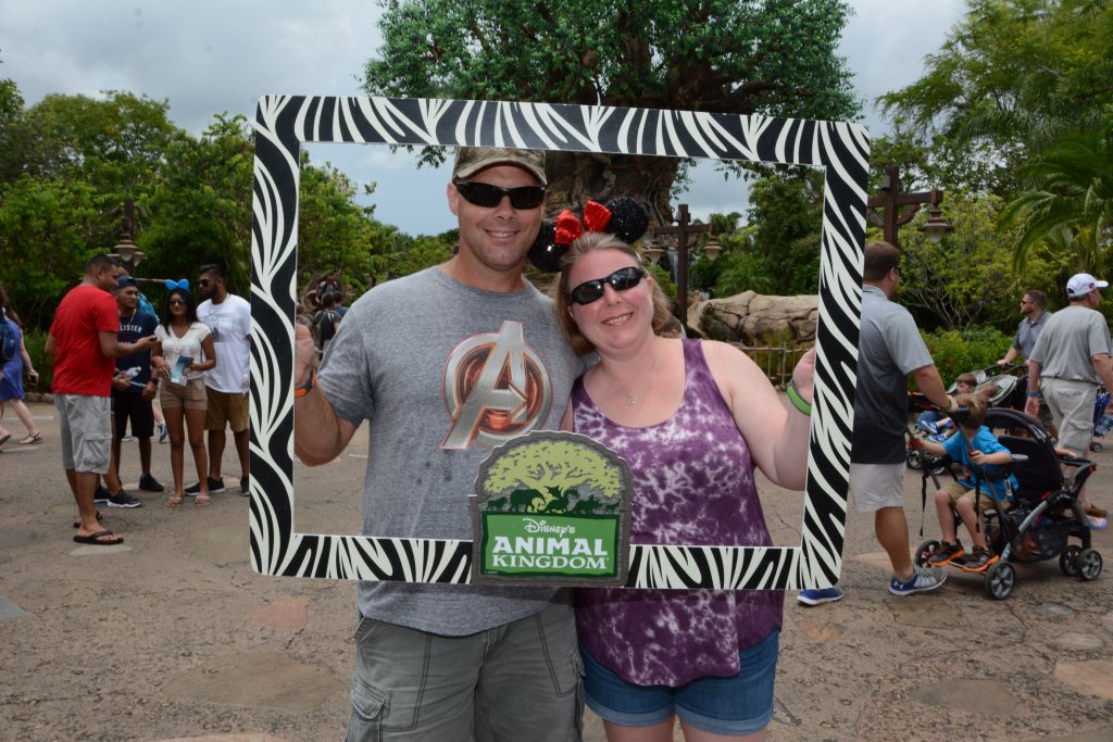 Husband and wife holding "Animal Kingdom" sign in front of the Tree of Life in Animal Kingdom