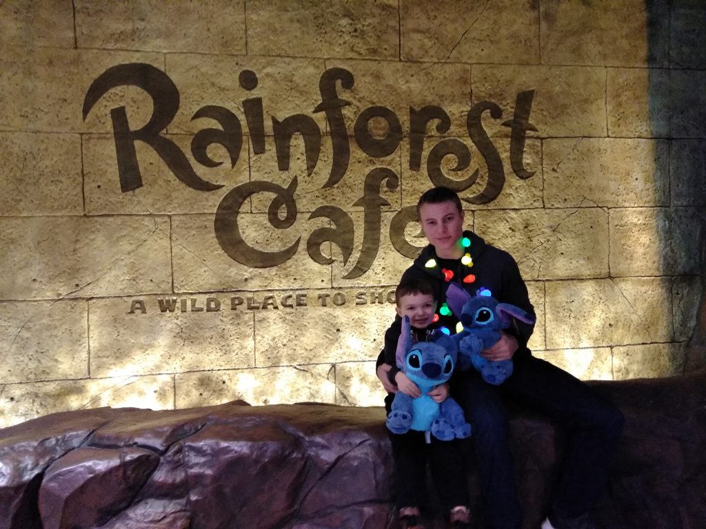 Nephew and uncle wearing Christmas necklaces and holding Stitch stuffed toys outside of Rainforest Cafe