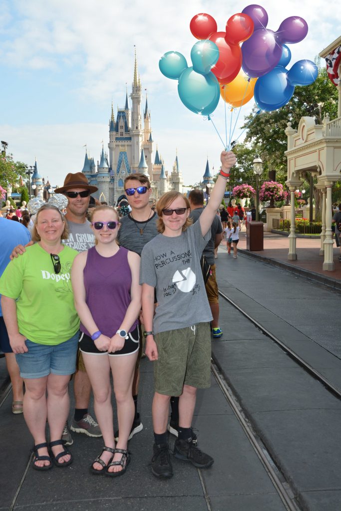 Family of five with son holding balloons in a Magic Shot at Magic Kingdom