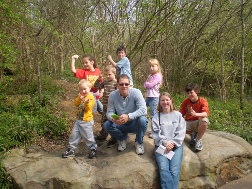 Mom, dad, and six children taking a picture on a rock at a local zoo