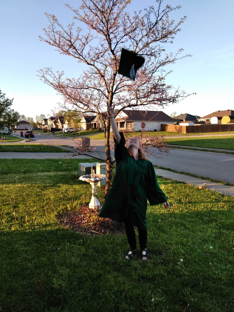 Girl in graduation gown throwing graduation cap